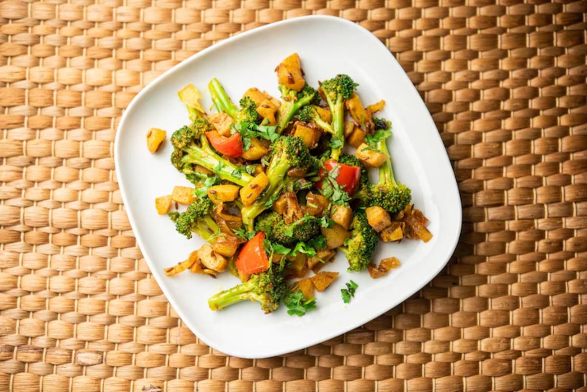 A vibrant dish of sautéed broccoli, red bell peppers, and diced potatoes garnished with fresh herbs on a white plate.