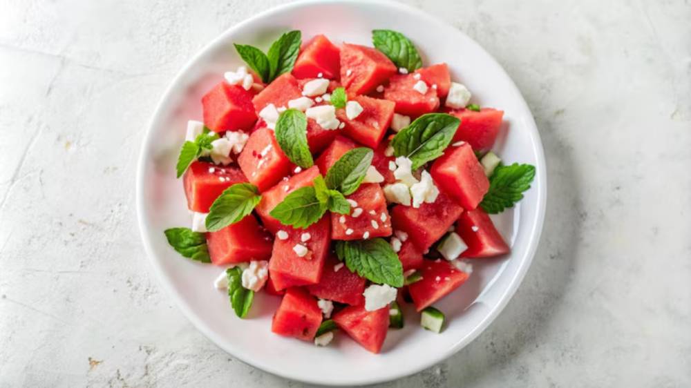 Fresh watermelon cubes topped with crumbled feta cheese and mint leaves on a white plate, garnished for a refreshing summer salad.