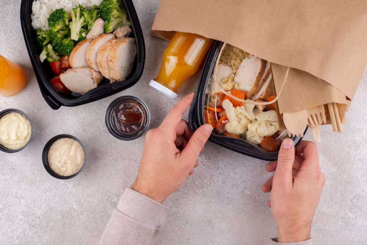 A person unpacks a healthy meal of rice, chicken, and vegetables, surrounded by sauces and drinks, ready to enjoy.