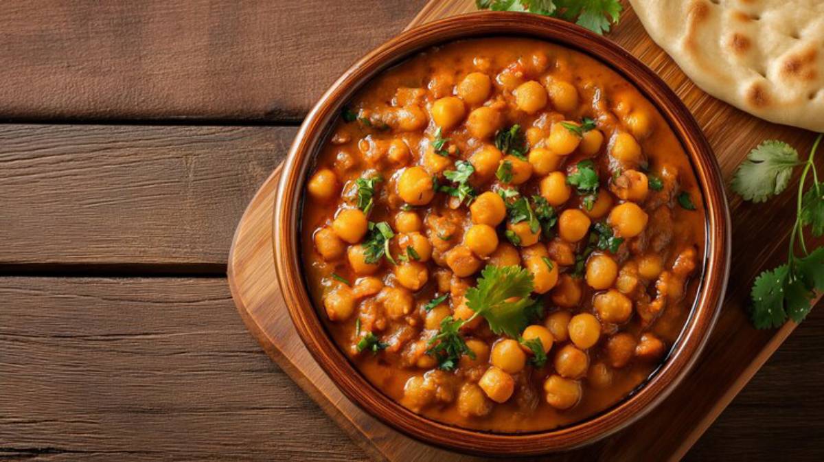 A bowl of flavorful chickpea curry topped with fresh cilantro, accompanied by a piece of naan bread on a wooden surface.