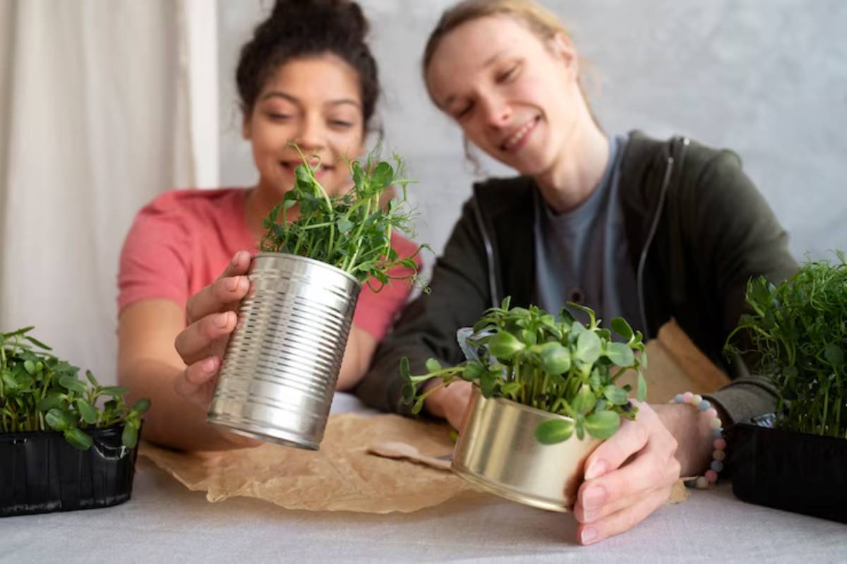 Two people hold potted plants in metal cans, showcasing their indoor gardening. Several green plants are arranged on a table.