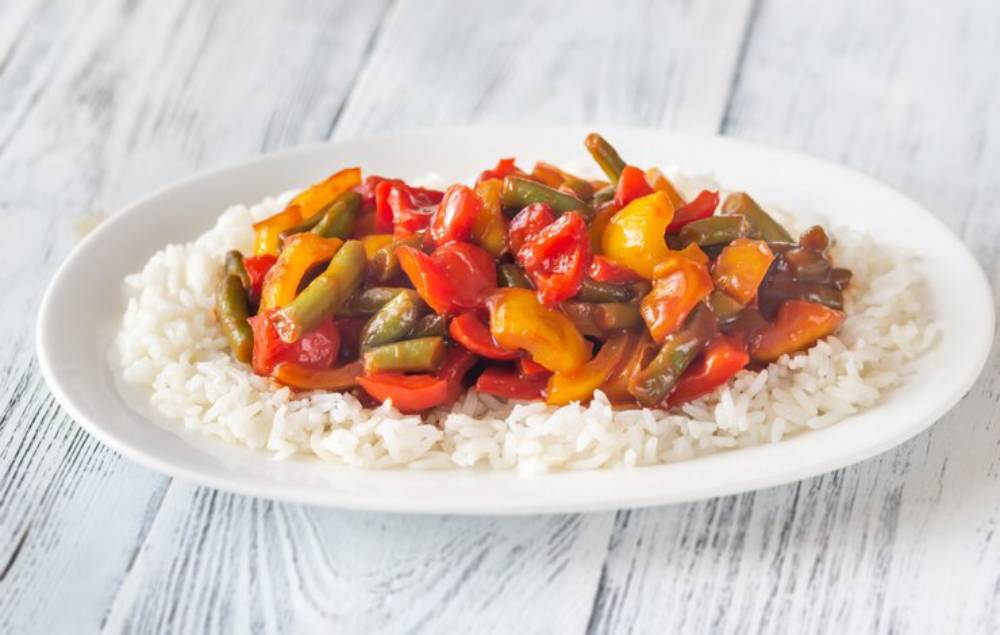 A plate of white rice topped with a colorful mix of sautéed bell peppers and green beans in a savory sauce.