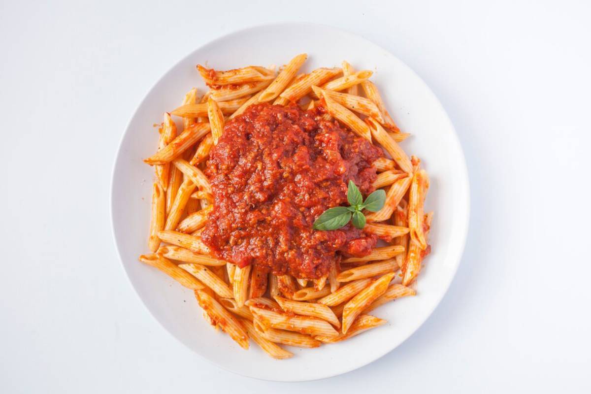 A plate of penne pasta topped with rich red tomato sauce and garnished with a fresh basil leaf.