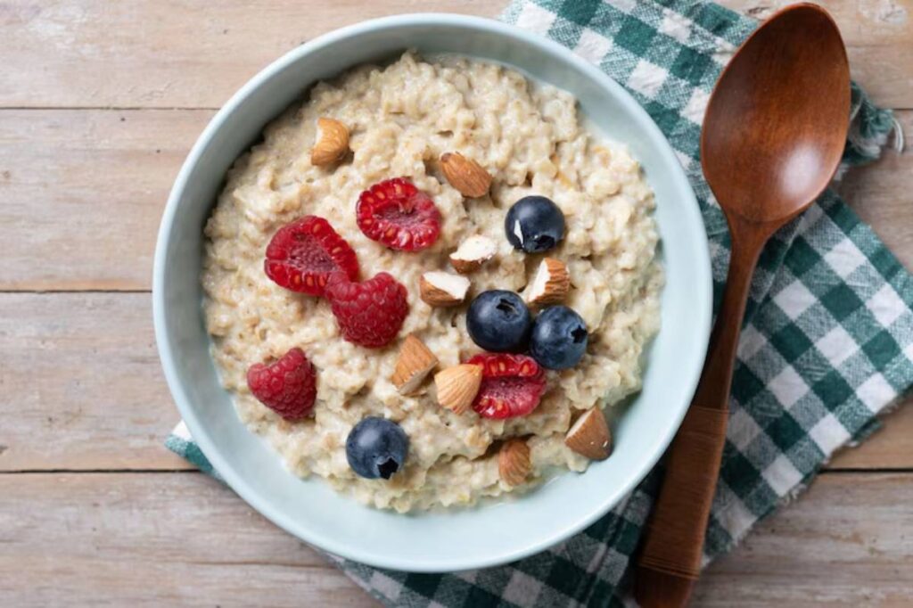 A bowl of oatmeal topped with raspberries, blueberries, and chopped almonds, resting on a checkered cloth with a wooden spoon nearby.