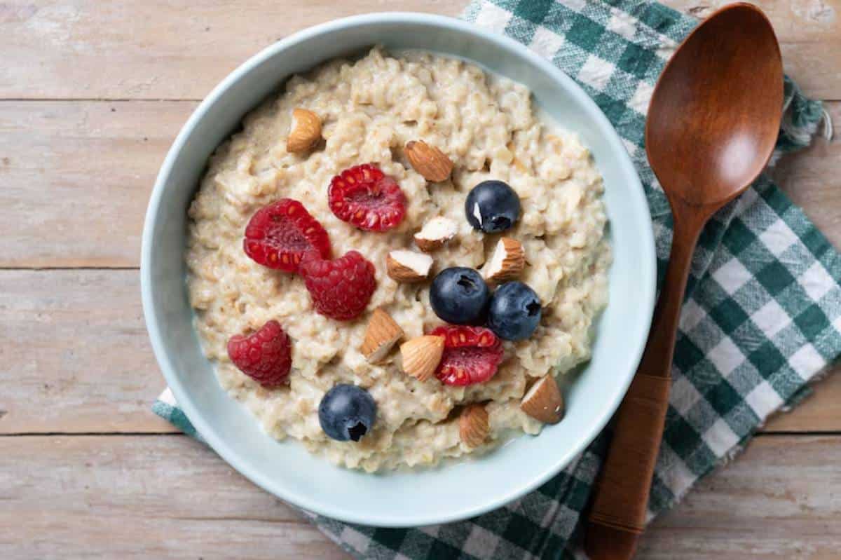 A bowl of oatmeal topped with raspberries, blueberries, and chopped almonds, resting on a checkered cloth with a wooden spoon nearby.