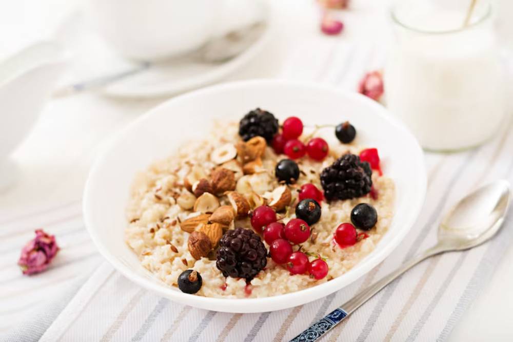A bowl of oatmeal topped with mixed berries and nuts, served on a striped tablecloth with a spoon and a glass of milk nearby.