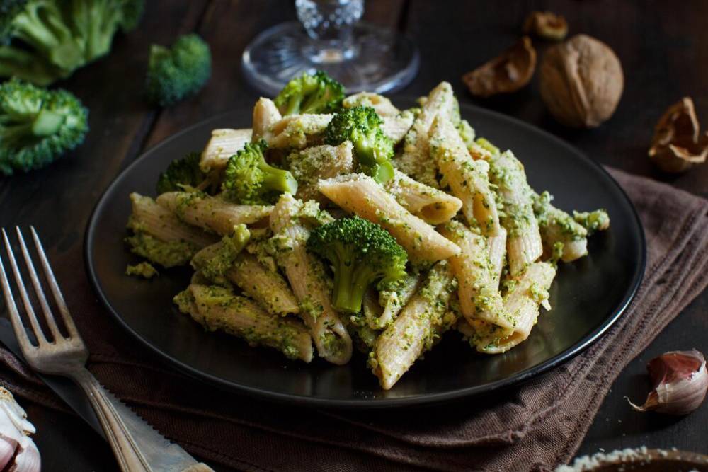 A plate of penne pasta mixed with vibrant green broccoli and a creamy pesto sauce, served on a rustic dark wooden table.
