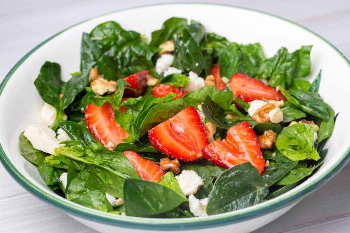 A fresh spinach salad topped with sliced strawberries, walnuts, and crumbled feta cheese in a white bowl.