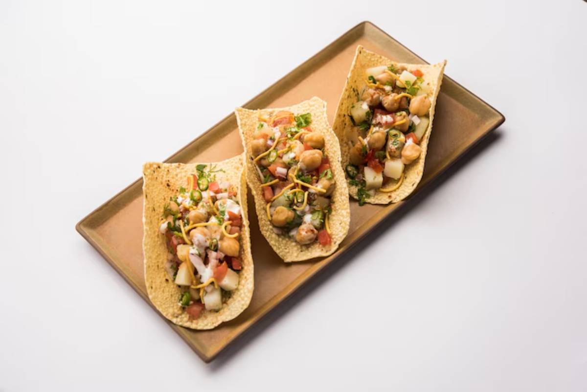Three colorful tacos filled with chickpeas, diced vegetables, and garnished with herbs, served on a bronze platter.