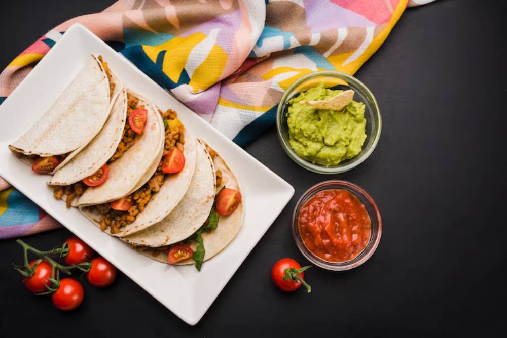 Three colorful tacos filled with chickpeas, diced vegetables, and garnished with herbs, served on a bronze platter.