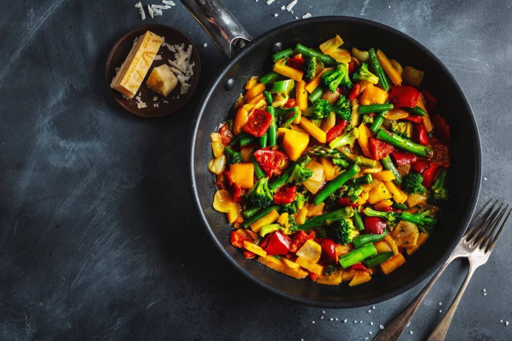 A vibrant stir-fry of colorful vegetables, including bell peppers, broccoli, and asparagus, served in a black skillet with cheese on the side.