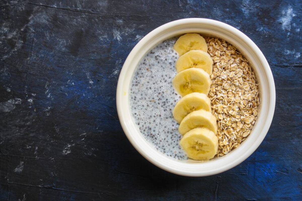 A bowl with chia pudding, sliced bananas, and rolled oats, presented against a dark blue textured background.