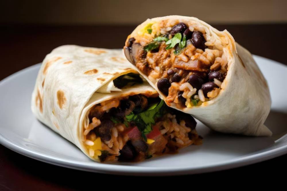 Two delicious wraps filled with black beans, rice, tomatoes, and fresh greens, served on a white plate.