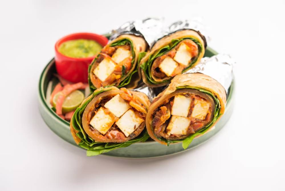 A plate of three wrapped tofu rolls with vegetables, served with a side of green sauce and lime wedges.